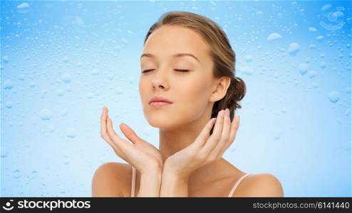 beauty, people, moisturizing, skin care and health concept - young woman face and hands over water drops on blue background