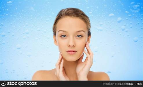 beauty, people, moisturizing, skin care and health concept - young woman with bare shoulders touching her face over water drops on blue background