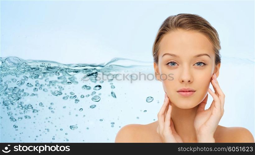 beauty, people, moisturizing, skin care and health concept - young woman with bare shoulders touching her face over water splash background