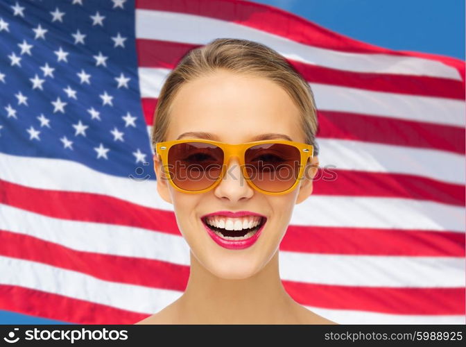 beauty, people, nationality and patriotism concept - smiling young woman in sunglasses with pink lipstick on lips over american flag background