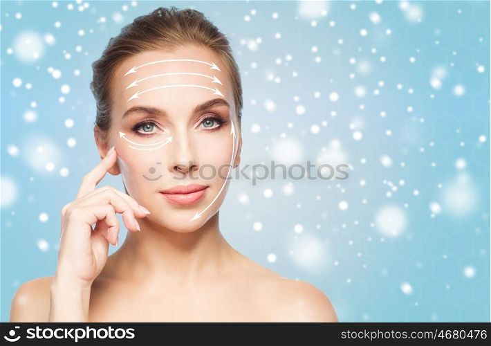 beauty, people , plastic surgery and anti-age concept - beautiful young woman with lifting arrows on face over blue background and snow