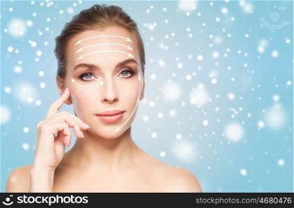 beauty, people , plastic surgery and anti-age concept - beautiful young woman with lifting arrows on face over blue background and snow