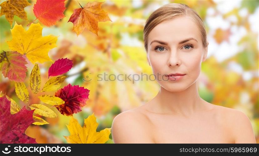 beauty, people, season and health concept - beautiful young woman face over autumn leaves background