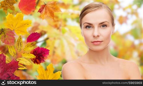 beauty, people, season and health concept - beautiful young woman face over autumn leaves background