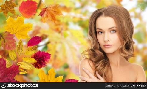 beauty, people, season and health concept - beautiful young woman face with long curly hair over autumn leaves background
