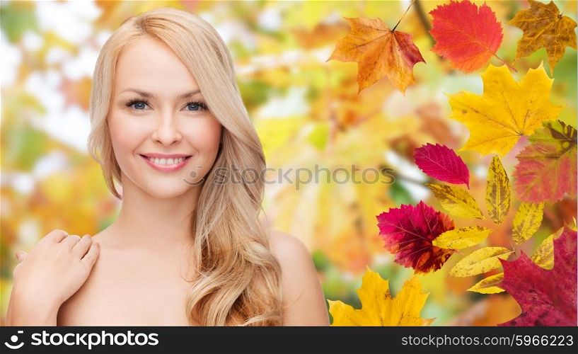 beauty, people, season and health concept - beautiful young woman face with long blonde hair over autumn leaves background