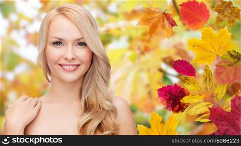 beauty, people, season and health concept - beautiful young woman face with long blonde hair over autumn leaves background