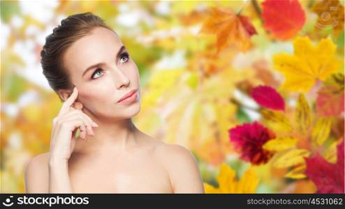 beauty, people, season and health concept - beautiful young woman touching her face over autumn leaves background