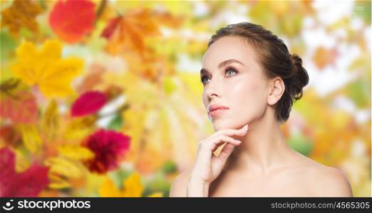 beauty, people, season and health concept - beautiful young woman touching her face over autumn leaves background