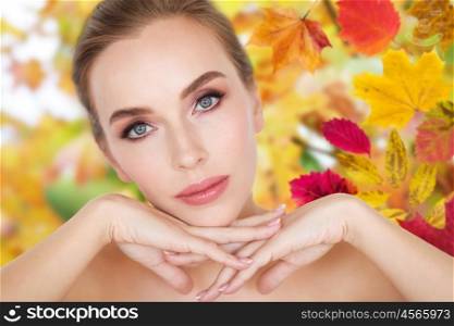 beauty, people, season, season and bodycare concept -beautiful young woman face and hands over autumn leaves background