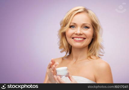 beauty, people, skincare and cosmetics concept - happy middle aged woman with cream jar over violet background