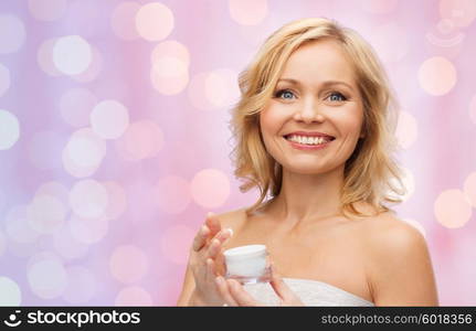 beauty, people, skincare and cosmetics concept - happy middle aged woman with cream jar over pink holidays lights background