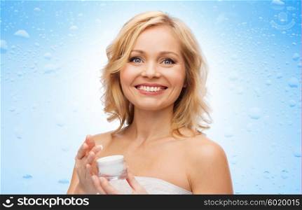 beauty, people, skincare and cosmetics concept - happy middle aged woman with cream jar over water drops on blue background