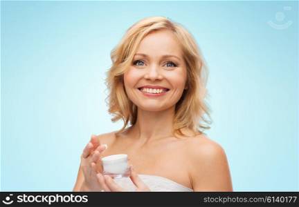 beauty, people, skincare and cosmetics concept - happy middle aged woman with cream jar over blue background