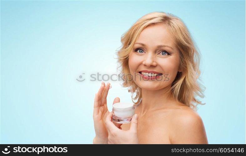 beauty, people, skincare and cosmetics concept - happy woman applying cream to her face over blue background
