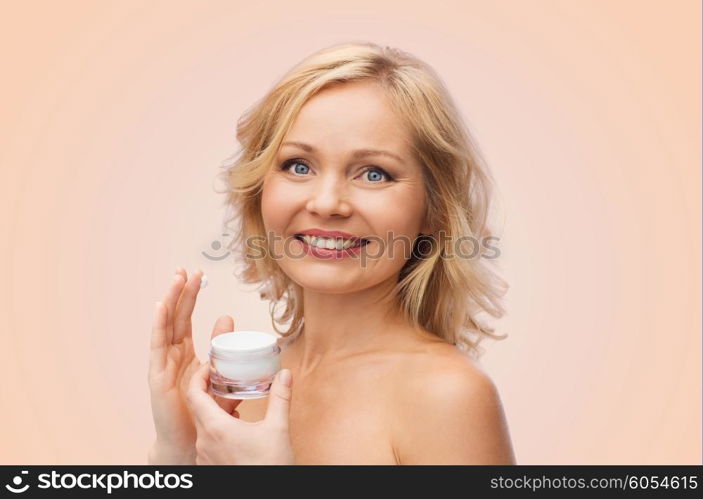 beauty, people, skincare and cosmetics concept - happy woman applying cream to her face over beige background