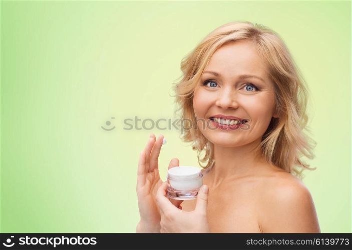 beauty, people, skincare and cosmetics concept - happy woman applying cream to her face over green natural background
