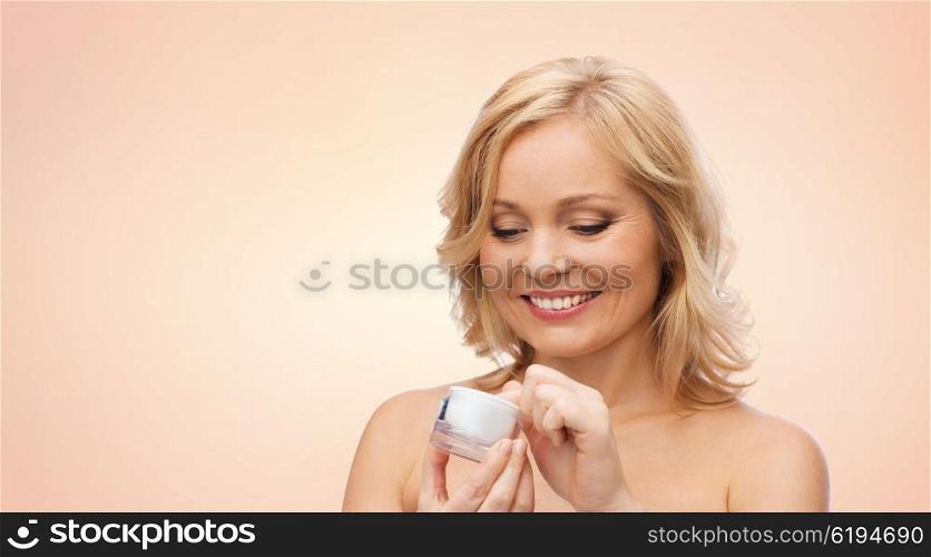 beauty, people, skincare and cosmetics concept - happy woman with cream jar over beige background