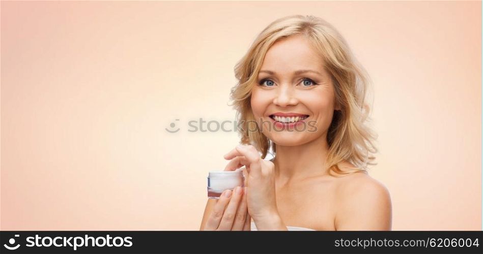 beauty, people, skincare and cosmetics concept - happy woman with cream jar over beige background