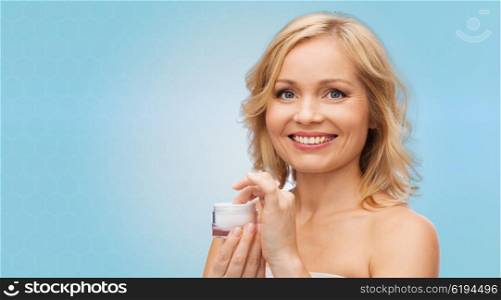 beauty, people, skincare and cosmetics concept - happy woman with cream jar over blue background