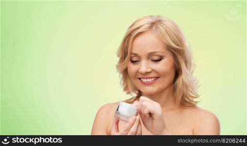 beauty, people, skincare and cosmetics concept - happy woman with cream jar over green natural background