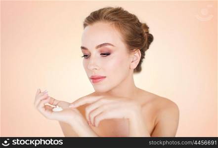 beauty, people, skincare and cosmetics concept - happy young woman with moisturizing cream on hand over beige background