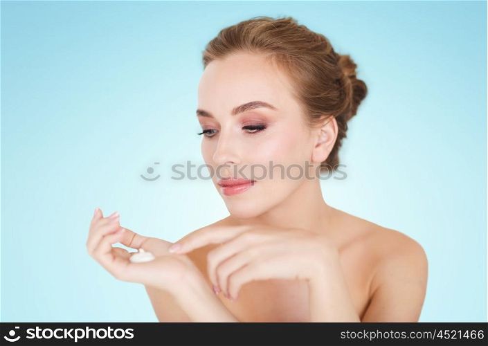 beauty, people, skincare and cosmetics concept - happy young woman with moisturizing cream on hand over blue background