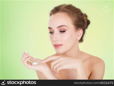 beauty, people, skincare and cosmetics concept - happy young woman with moisturizing cream on hand over green background