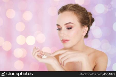 beauty, people, skincare and cosmetics concept - happy young woman with moisturizing cream on hand over rose quartz and serenity lights background