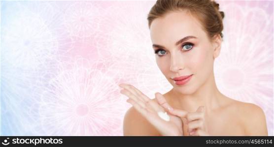 beauty, people, skincare and cosmetics concept - happy young woman with moisturizing cream on hand over rose quartz and serenity patterned background