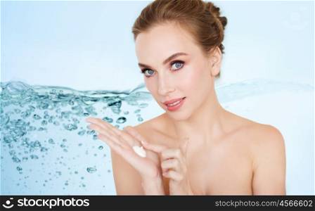 beauty, people, skincare and cosmetics concept - happy young woman with moisturizing cream on hand over blue background with water splash