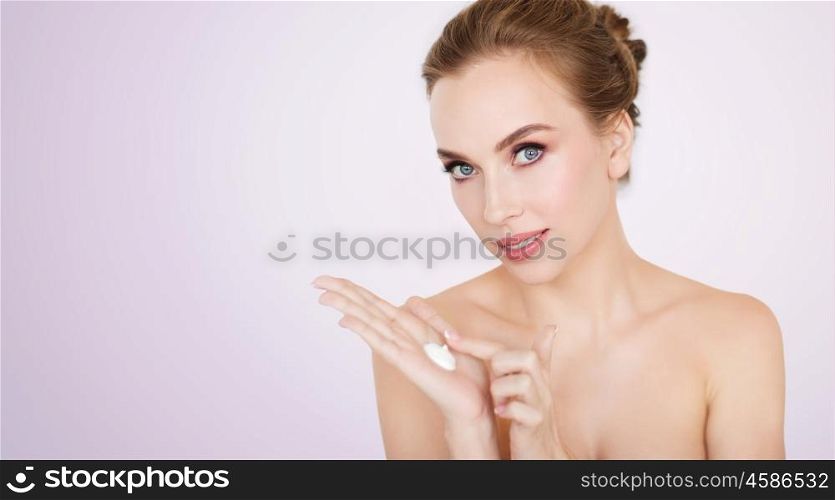 beauty, people, skincare and cosmetics concept - happy young woman with moisturizing cream on hand over violet background