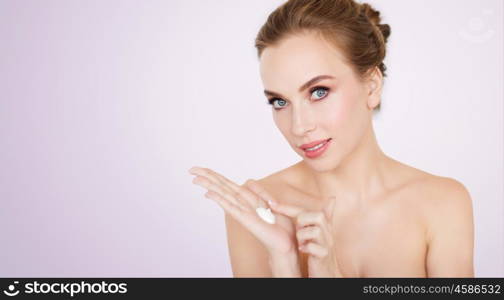 beauty, people, skincare and cosmetics concept - happy young woman with moisturizing cream on hand over violet background