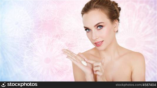 beauty, people, skincare and cosmetics concept - happy young woman with moisturizing cream on hand over rose quartz and serenity pattern background