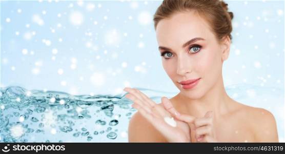 beauty, people, skincare and cosmetics concept - happy young woman with moisturizing cream on hand over water splash bubbles on blue background and snow