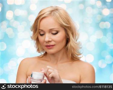 beauty, people, skincare and cosmetics concept - middle aged woman with cream jar over blue holidays lights background