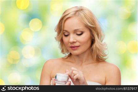 beauty, people, skincare and cosmetics concept - middle aged woman with cream jar over green summer lights background