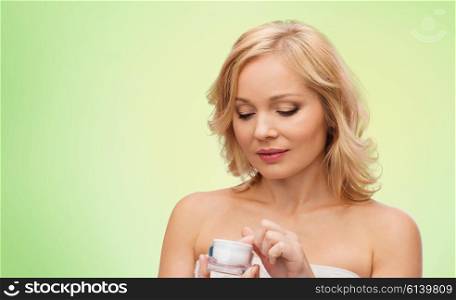 beauty, people, skincare and cosmetics concept - middle aged woman with cream jar over green natural background