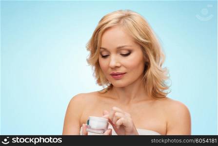 beauty, people, skincare and cosmetics concept - middle aged woman with cream jar over blue background