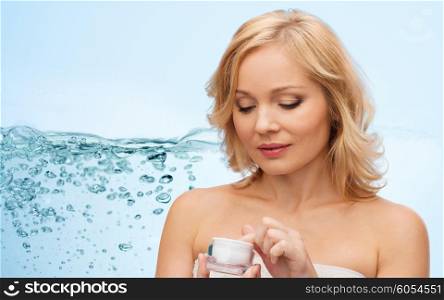 beauty, people, skincare and cosmetics concept - middle aged woman with moisturizing cream jar over blue background and water splash