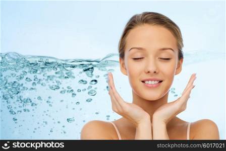beauty, people, skincare and health concept - smiling young woman face and hands over water splash on blue background