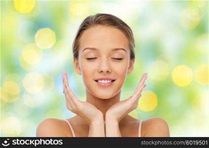 beauty, people, skincare and health concept - smiling young woman face and hands over green lights background