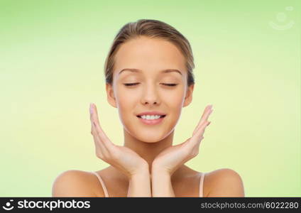 beauty, people, skincare and health concept - smiling young woman face and hands over green natural background