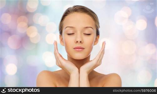beauty, people, skincare and health concept - young woman face and hands over purple holidays lights background
