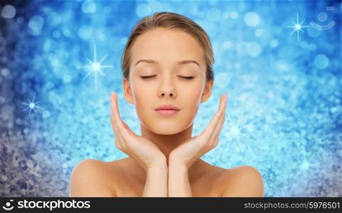 beauty, people, skincare and health concept - young woman face and hands over blue holidays lights or glitter background