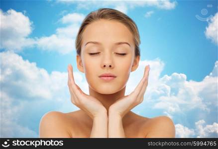 beauty, people, skincare and health concept - young woman face and hands over blue sky and clouds background