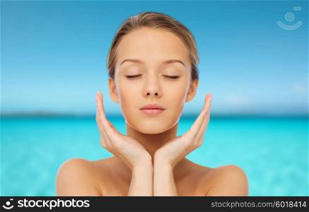 beauty, people, skincare and health concept - young woman face and hands over blue sea and sky background
