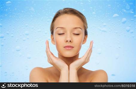 beauty, people, skincare and health concept - young woman face and hands over water drops on blue background