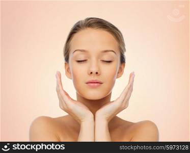 beauty, people, skincare and health concept - young woman face and hands over beige background