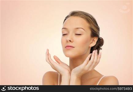 beauty, people, skincare and health concept - young woman face and hands over beige background